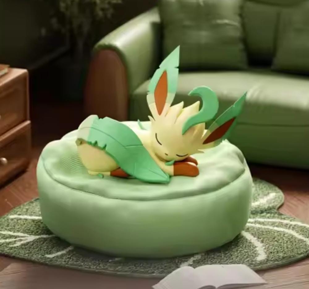 Sleeping Leafeon figure with detailed ear and tail foliage resting peacefully on a moss-green circular cushion, part of the Eeveelution Oyasumi collection.